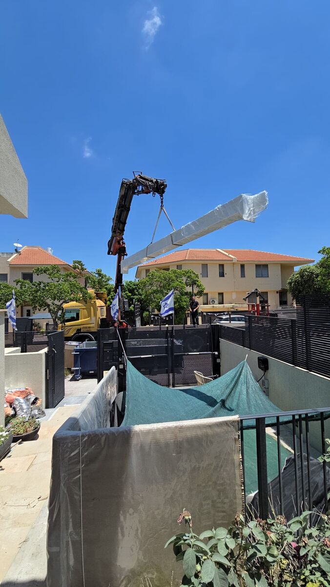 מנוף מרים קורת פלדה לבנה וארוכה מעל חצר בית