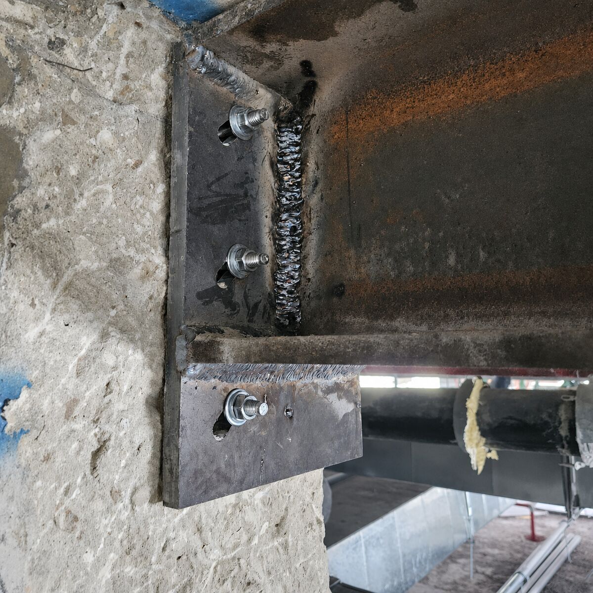 תקריב של ריתוך פלטת פלדה וברגי עיגון בקצה קורה