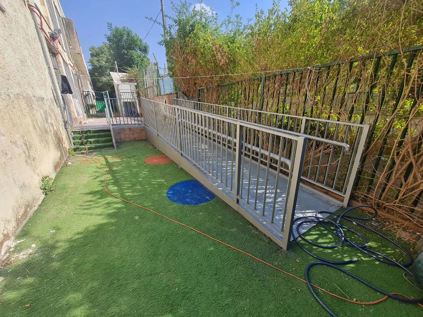 כבש נגישות עם משטח מתכת ומעקות בטיחות בחצר מבנה קיים